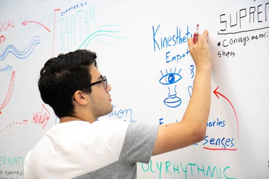 A man wearing eyeglasses writes educational content on a whiteboard.
