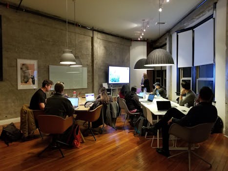 Diverse team collaborating in a modern office setting with laptops and presentation screen.