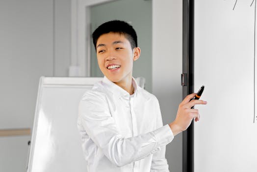 Smiling young man in smart casual attire giving a presentation using a whiteboard indoors.