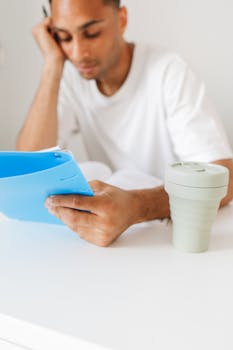 A man intently reading documents with a coffee cup at a bright, minimalistic desk.